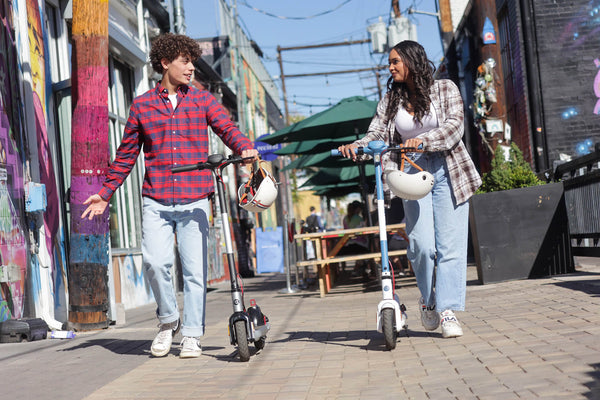 Two people walking with GOTRAX Apex LE Casual Electric Scooters