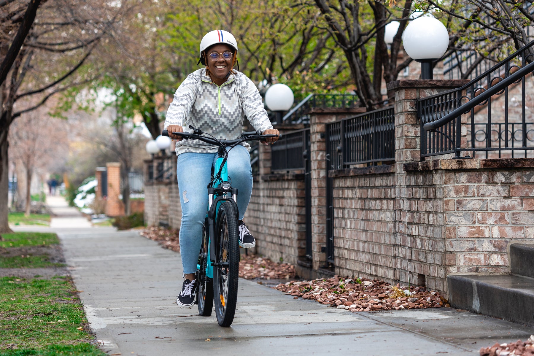Woman riding GOTRAX Teal Emerge Electric Bike for Adults on a sidewalk. 