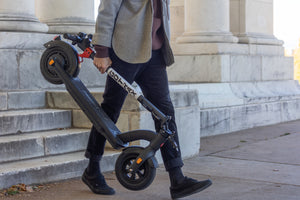 Man Carrying GOTRAX Black G4 Foldable Commuter Electric Scooter for Adults in the Folded Position