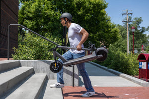 Man carrying a GOTRAX G5 Commuter Electric Scooter with Front Wheel Suspension in the Folded Position