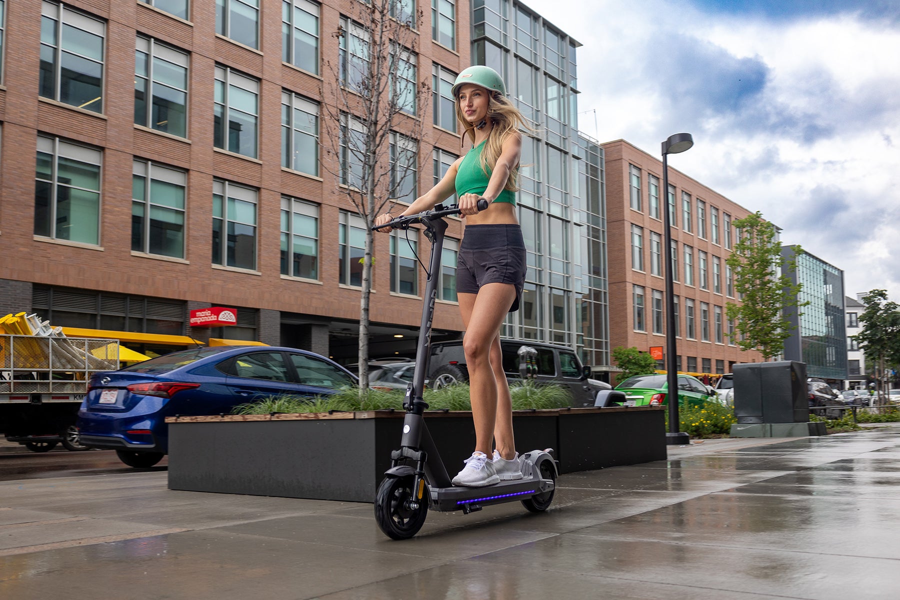 Woman riding a GOTRAX G6 Commuter Electric Scooter for Adults down the sidewalk