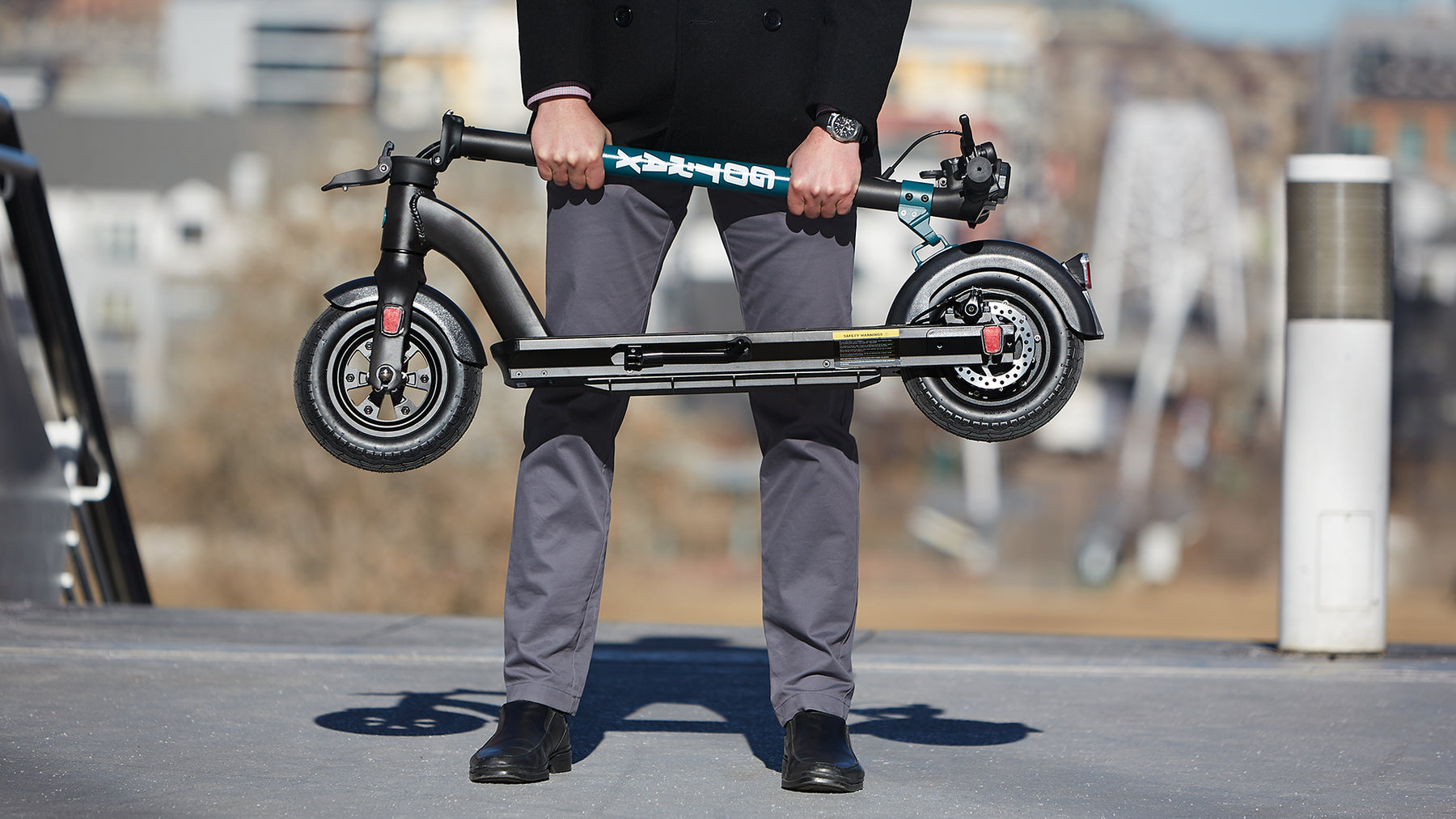 Man holding a GOTRAX Black GMAX Long-Distance Electric Scooter for Adults in the Folded Position. 