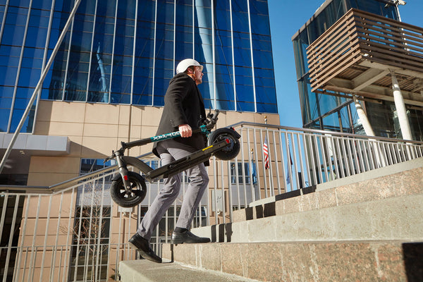 Man carrying the GOTRAX GMAX Ultra Commuter Electric Scooter in the Folded Position Up a Flight of Stairs