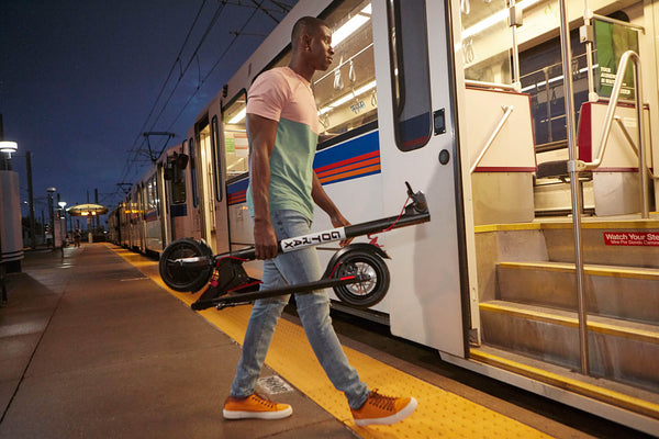 Man carrying a GOTRAX GXL V2 Casual Electric Scooter in the Folded Position onto a Train