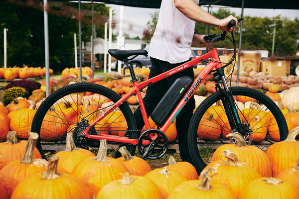 Man walking with a GOTRAX Traveler All-Terrain Electric Bike for Adults with Front Wheel Suspension through a pumpkin patch